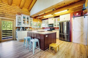 A kitchen with wooden beams, a central island, bar stools, and a view through a window. - The Cub Inn - Groveland (Groveland)