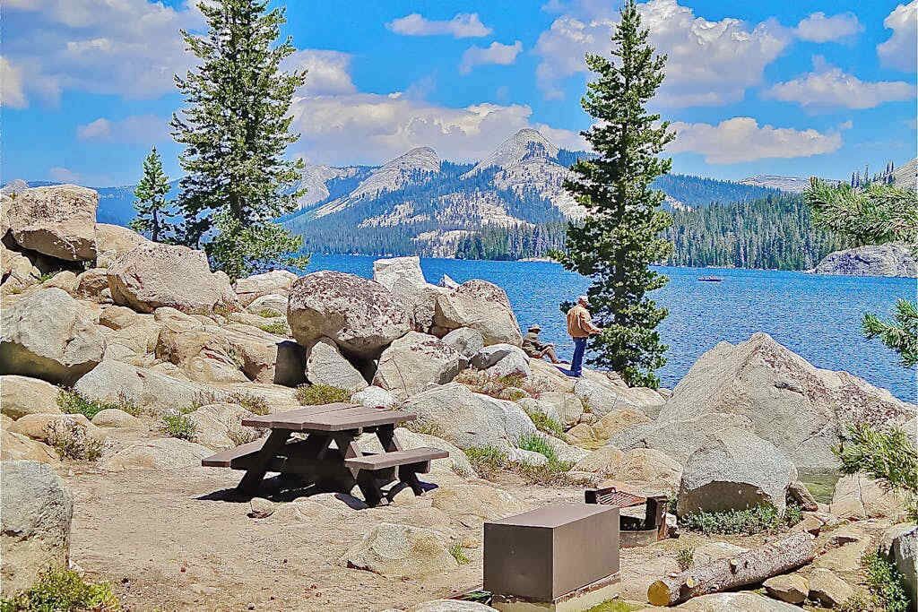 A rocky lakeside area with picnic tables and a person standing by the water.