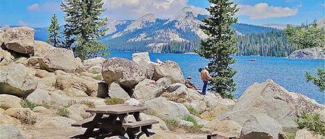 A rocky lakeside area with picnic tables and a person standing by the water.