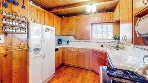 A compact kitchen with wooden cabinets, a white refrigerator, a stove, and a window providing natural light. - Mountain Memories - Musick Meadows (Shaver Lake)