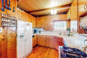 A compact kitchen with wooden cabinets, a white refrigerator, a stove, and a window providing natural light. - Mountain Memories - Musick Meadows (Shaver Lake)