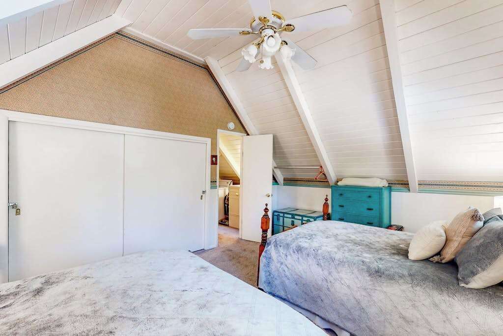 Un dormitorio con techo inclinado, ventilador de techo y cama con colcha estampada.