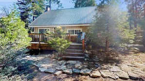 A cabin with a metal roof, wooden deck, and stone steps leading to the entrance. - Mountain Memories - Musick Meadows (Shaver Lake)