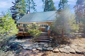 A cabin with a metal roof, wooden deck, and stone steps leading to the entrance. - Mountain Memories - Musick Meadows (Shaver Lake)