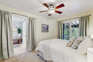 Une chambre à coucher avec un lit, un ventilateur de plafond, une fenêtre avec des rideaux et une porte donnant sur une autre pièce.