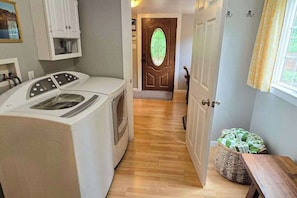 A laundry area with a washing machine and dryer, a wooden floor, a door with a green glass window, and a wicker basket with towels. - Cabin On The Flume - Avery (Avery)