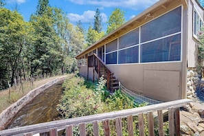 A building with a wooden deck, a stone wall, and a view of a water feature. - Cabin On The Flume - Avery (Avery)