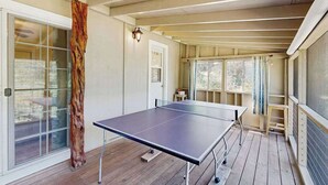 Una mesa de ping pong en una habitación con piso de madera, un vidrio y una ventana con cortinas.