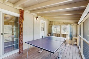 A ping pong table in a room with a wooden floor, a glass door, and a window with curtains. - Cabin On The Flume - Avery (Avery)