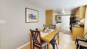 Un comedor con una mesa y sillas de madera, una cocina con armarios de madera y un cuadro en la pared.