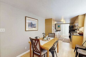 A dining area with a wooden table and chairs, a kitchen with wooden cabinets, and a framed picture on the wall. - Cabin On The Flume - Avery (Avery)