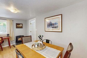 Un coin repas avec une table en bois, des chaises, un tableau encadré au mur et une fenêtre avec des rideaux.