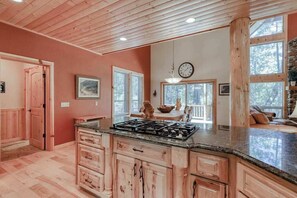 A spacious kitchen with wooden cabinets, a granite countertop, and a large island. There is a clock on the wall and a window with blinds. - Pinnacle Point - Granite Ridge (Shaver Lake)
