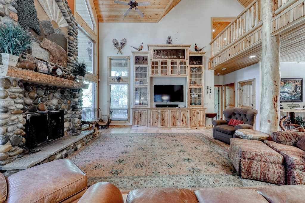 A spacious living room with a stone fireplace, a large flat-screen TV, and a multi-level wooden deck.