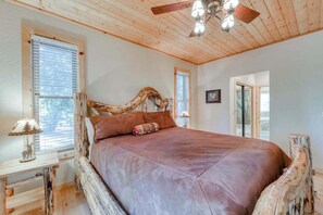 Een slaapkamer met een houten plafond, een bed met een hoofdbord van boomstammen en een raam met jaloezieën.
