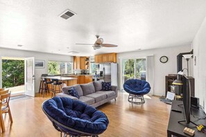 A spacious living area with a sofa, a blue chair, and a dining table. There is a kitchen in the background with wooden cabinets and a refrigerator. - Big Creek Hideaway - Pine Mountain Lake (Groveland)