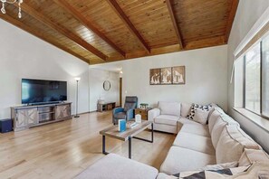 Ein geräumiges Wohnzimmer mit Holzboden, einem großen Flachbildfernseher, einer Sofagarnitur und einem Couchtisch.