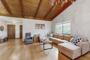 A spacious living room with a wooden ceiling, a large sofa set, a coffee table, and a view through a window. - Harmony Haven - Pine Mountain Lake (Groveland)
