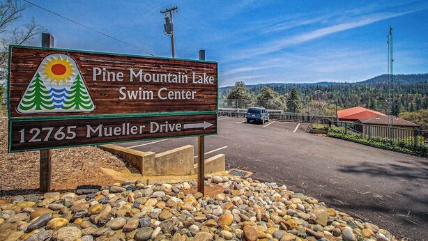 Ein Holzschild für das Pine Mountain Lake Schwimmzentrum mit einem Pfeil, der auf die Mueller Drive zeigt.