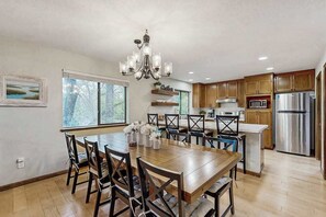 A modern kitchen with wooden cabinets, a stainless steel refrigerator, and a dining area with a wooden table and chairs. - Harmony Haven - Pine Mountain Lake (Groveland)