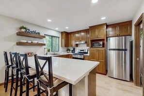 A modern kitchen with wooden cabinets, a stainless steel refrigerator, and a central island with chairs. - Harmony Haven - Pine Mountain Lake (Groveland)