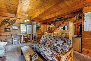 L’intérieur d’un chalet en bois, avec un canapé, une table à manger, des chaises et un escalier.