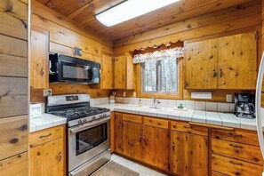 Eine Küchenzeile im Chalet-Stil mit Holdekor, einem Herd, einer Mikrowelle und einem Fenster mit Vorhang.