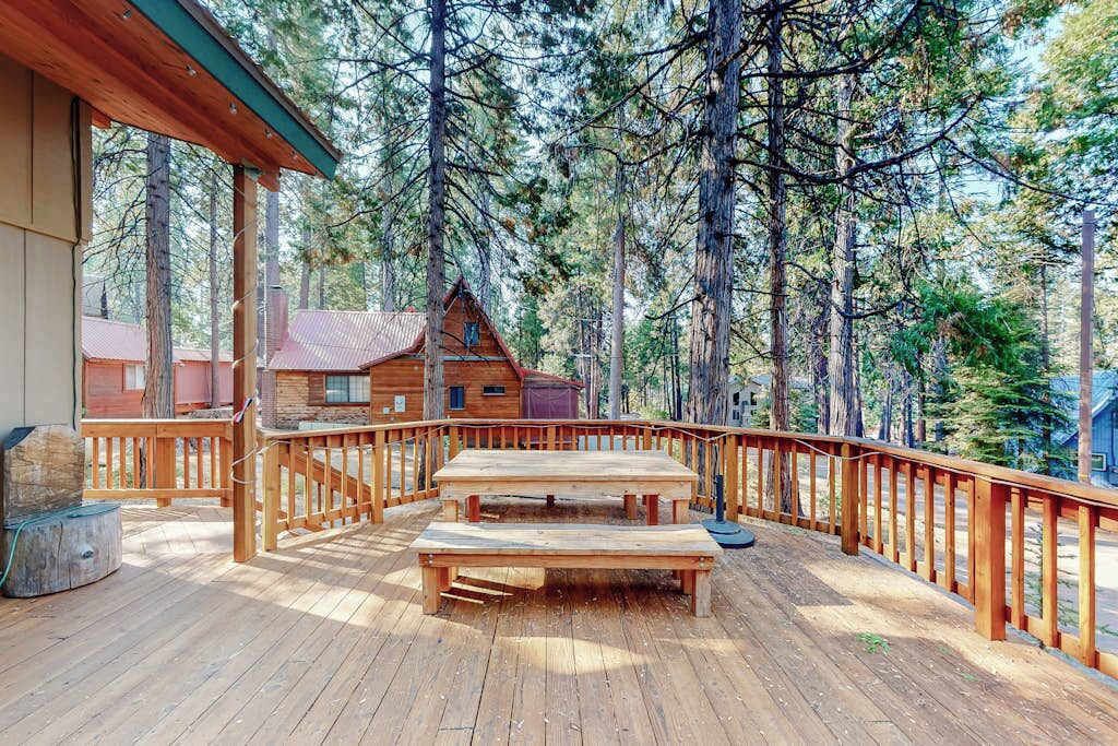 En träaltan med picknickbord, omgiven av ett trästaket, med utsikt över ett skogsområde.