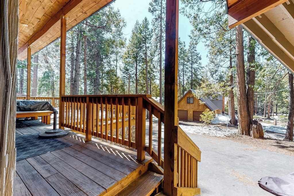 Eine Holzterrasse mit Geländer, einer Bank und einer kleinen Holzhütte in bewaldeter Landschaft.