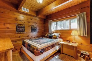 Ein Schlafzimmer einer Holzhütte mit einem Bett, einem Nachttisch, einem Fenster mit Vorhängen und einer Hängelampe.