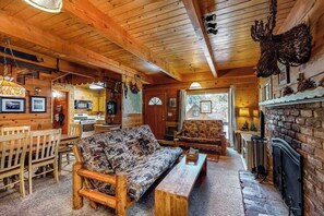L’intérieur d’un chalet confortable, avec des murs en rondins de bois, un canapé en bois, une table à manger et une cheminée.