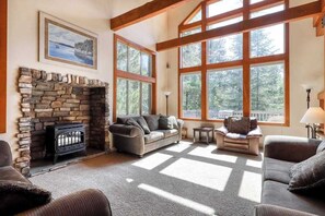 A cozy living room with a stone fireplace, large windows, and comfortable seating. - Alder Hill Hideaway - Wildflower Village (Shaver Lake)