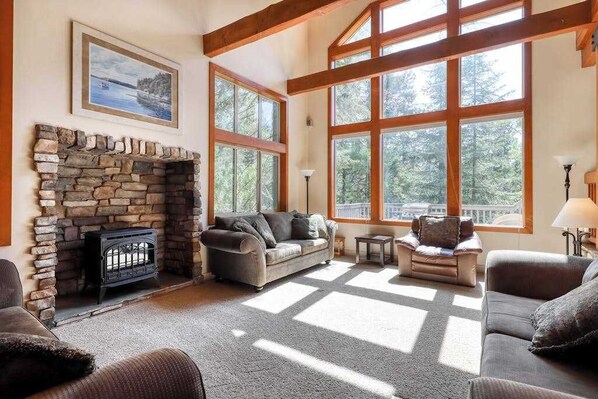 A cozy living room with a stone fireplace, large windows, and comfortable seating. - Alder Hill Hideaway - Wildflower Village (Shaver Lake)