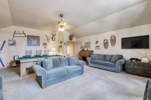 A living room with a pool table, two sofas, a television, and various wall decorations including antlers and a fireplace. - Alder Hill Hideaway - Wildflower Village (Shaver Lake)