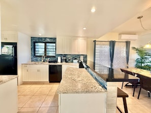 A modern kitchen with white cabinetry, a granite countertop, and a black refrigerator. - Sunset Oasis - 2Br Beach Front Condo (Christiansted)