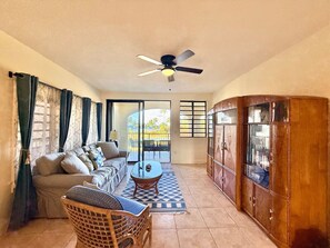 A living room with a sofa, a coffee table, a ceiling fan, and a wooden cabinet. - Sunset Oasis - 2Br Beach Front Condo (Christiansted)