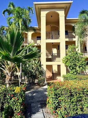 A multi-story hotel with balconies, surrounded by tropical vegetation and a paved pathway. - Sunset Oasis - 2Br Beach Front Condo (Christiansted)