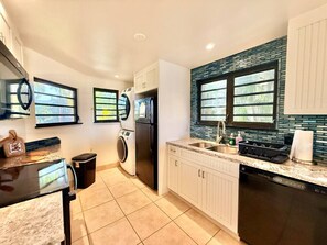 A modern kitchen with a built-in washer and dryer, a granite countertop, and a backsplash with blue tiles. - Sunset Oasis - 2Br Beach Front Condo (Christiansted)
