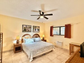 A bedroom with a bed, two bedside tables with lamps, a ceiling fan, a window with curtains, and a radiator. - Sunset Oasis - 2Br Beach Front Condo (Christiansted)