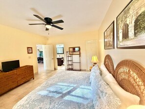 A bedroom with a bed, a ceiling fan, a television on a wooden dresser, and a door leading to another room. - Sunset Oasis - 2Br Beach Front Condo (Christiansted)