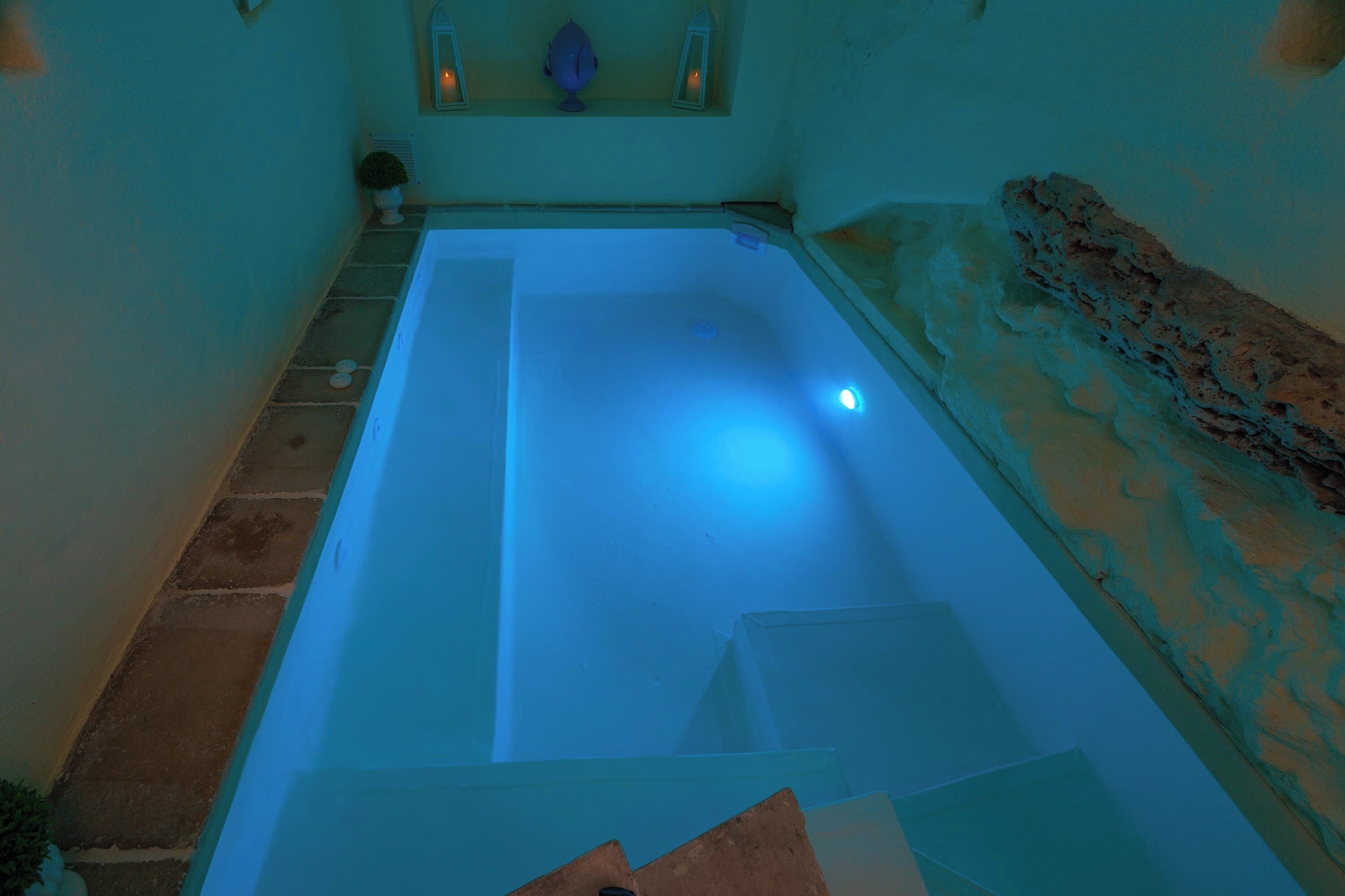 A spa bath with a blue light, a stone wall, and a small window with decorative items.
