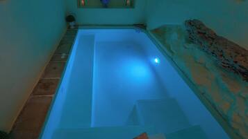 A spa bath with a blue light, a stone wall, and a small window with decorative items.