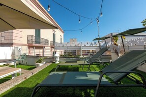 Un espace extérieur aménagé avec une pelouse, des chaises longues et un bâtiment doté d’un balcon.