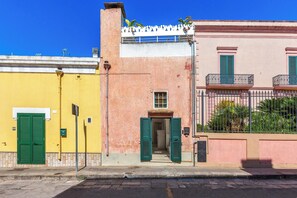 Une vue de rue avec un immeuble jaune, un immeuble rose doté d’un balcon et une porte verte.