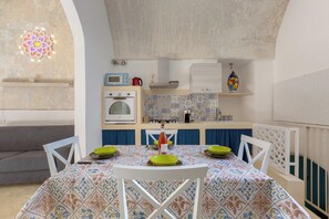 Un coin repas avec une table dressée pour quatre personnes, une cuisine en arrière-plan et un luminaire décoratif.