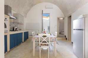 A compact kitchen with a dining area, featuring a central island, a built-in oven, and a refrigerator. - AquaTerrae by BarbarHouse (Alezio)