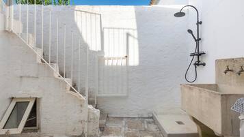 A small, enclosed outdoor space with a white wall, a metal staircase, a shower area, and a sink.
