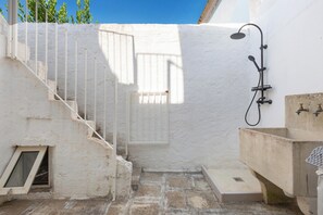 A small, enclosed outdoor space with a white wall, a metal staircase, a shower area, and a sink. - AquaTerrae by BarbarHouse (Alezio)