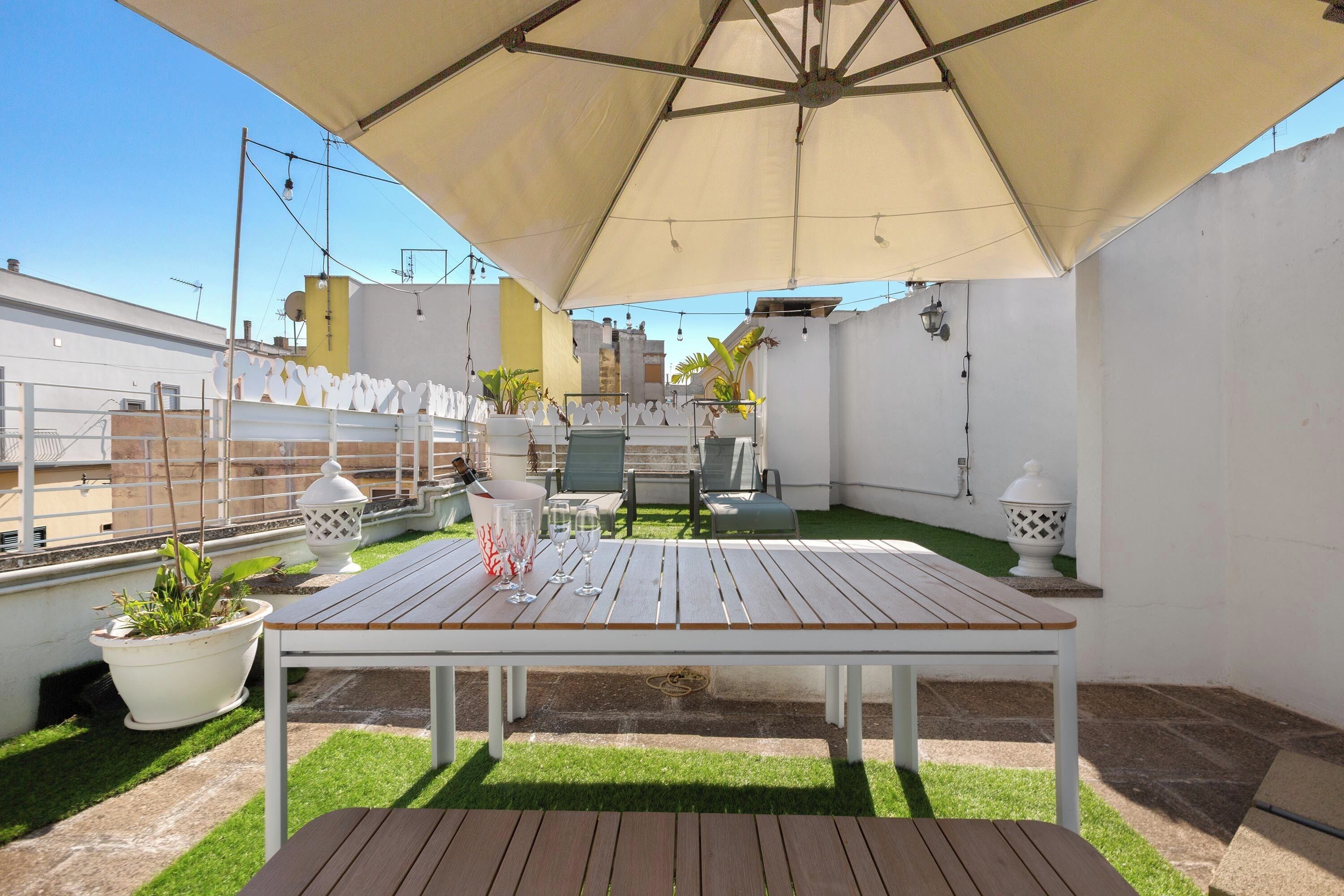 An outdoor patio with a wooden table, chairs, and a large umbrella providing shade.