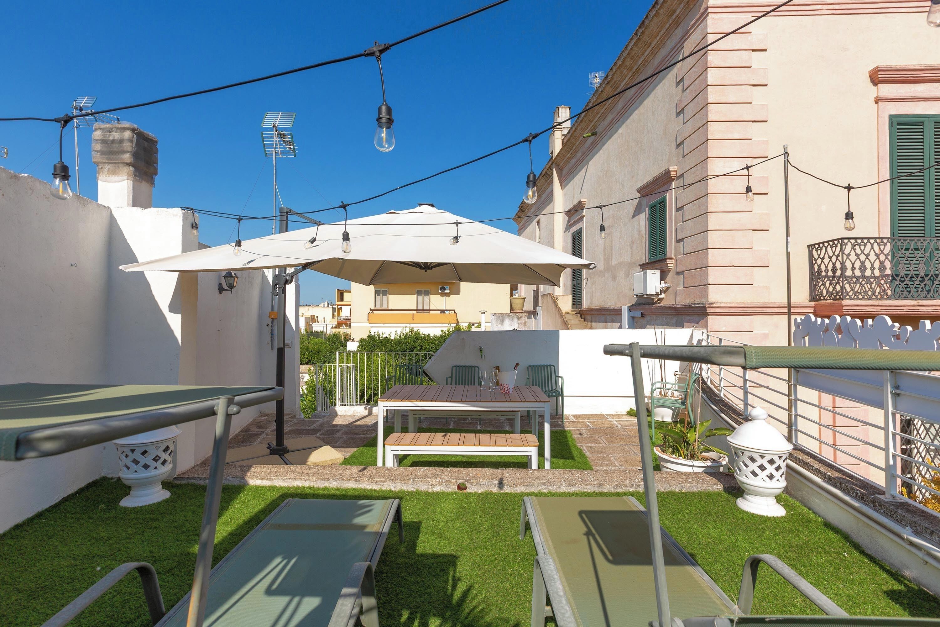 Un espace patio avec une table et des chaises, un parasol blanc et un petit jardin.